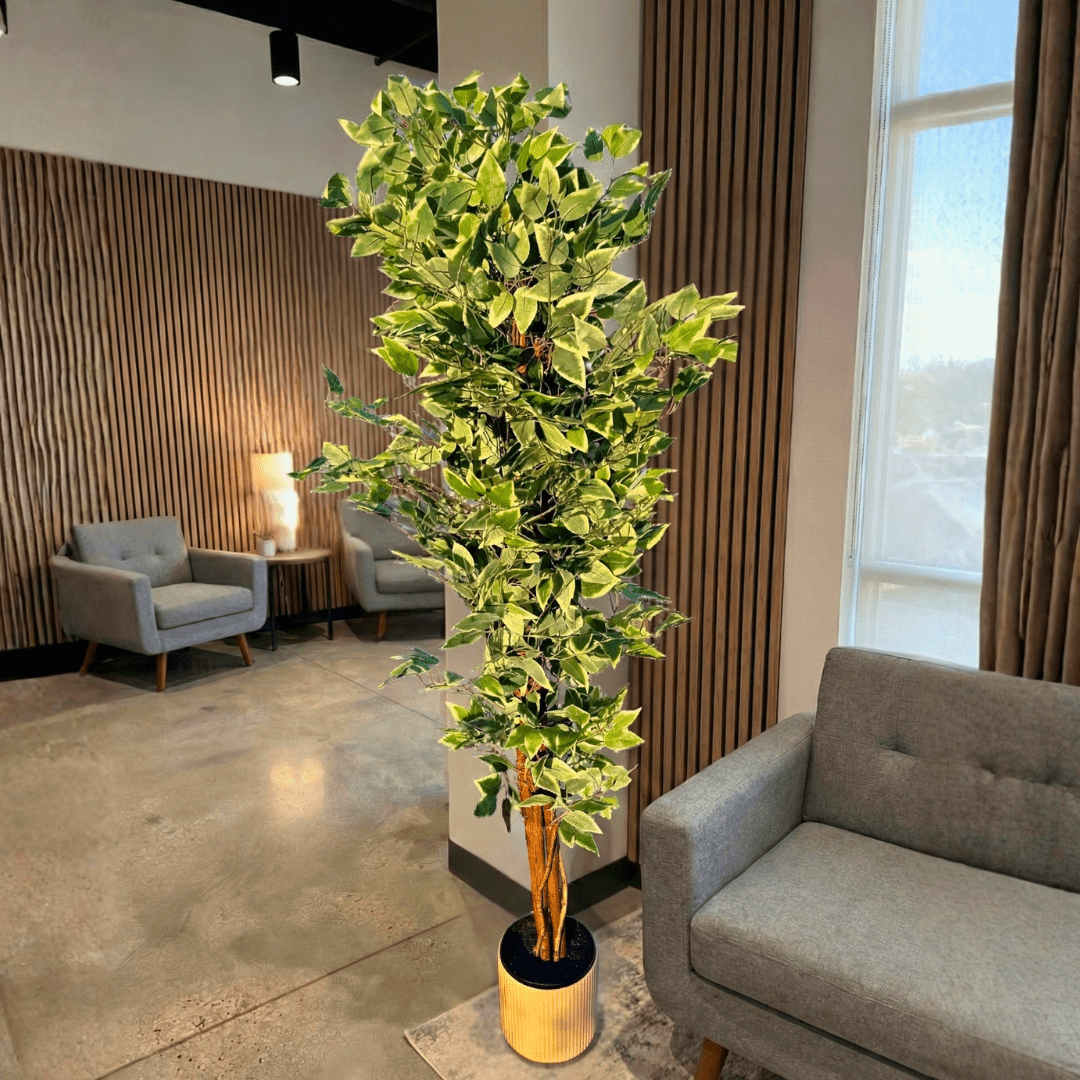 Tall artificial plant in a modern office setting with gray chairs and a large window.