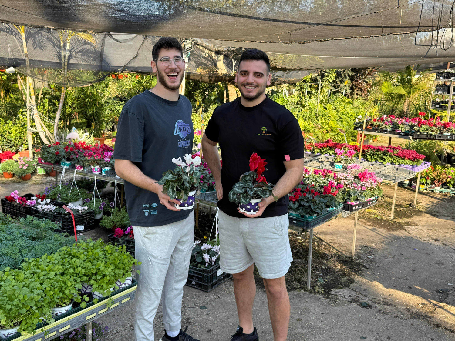 Two men holding potted plants in a garden center.