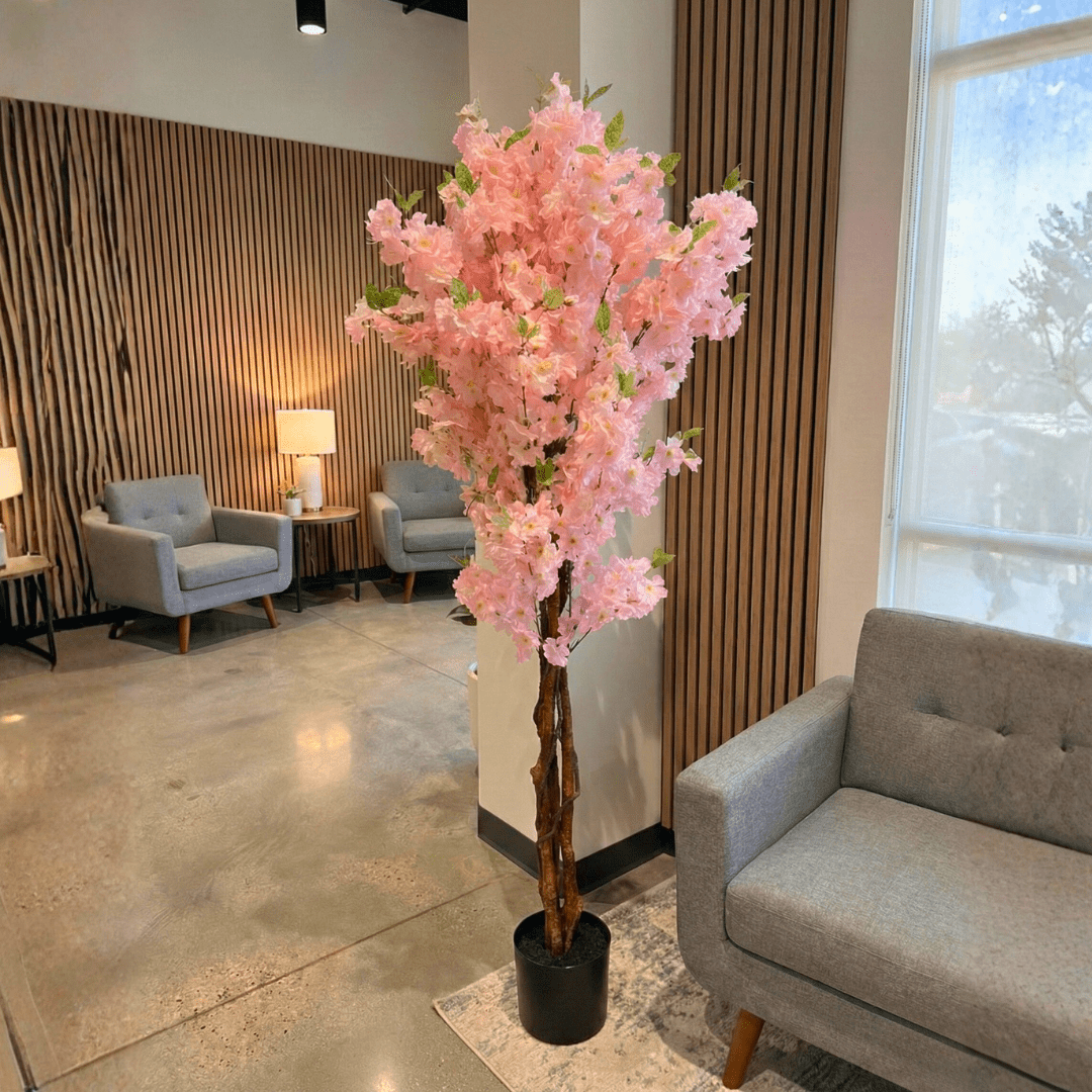 Pink artificial cherry blossom tree in a modern living room setting with gray sofa and chairs.