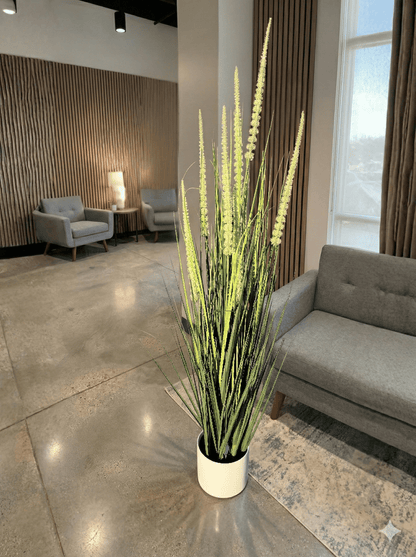 artifical plant in a white pot in a modern office setting with gray furniture and large windows.