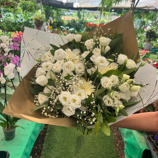 Bouquet of white flowers held by a person in a greenhouse setting
